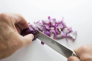 L’art de la découpe : Comment préparer une planche apéritive digne d’un grand chef ? Close-up of hands slicing purple onions on a white cutting board with a sharp knife.