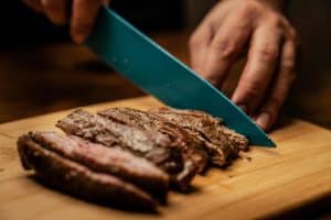 L’art de la découpe : Comment préparer une planche apéritive digne d’un grand chef ? Hands slicing tender, juicy grilled steak on a wooden board, showcasing a mouth-watering culinary scene.
