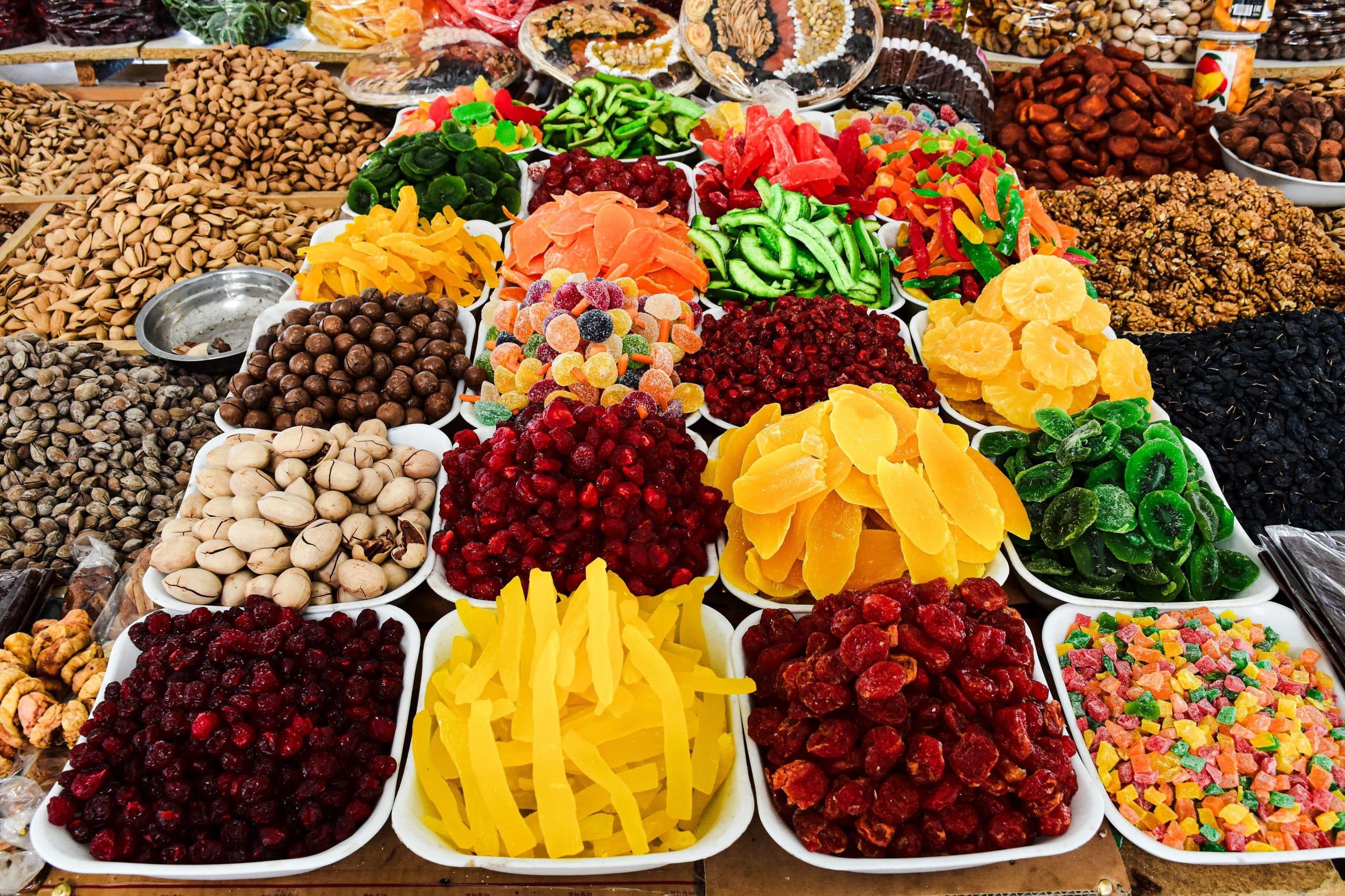 Color Foods : l'art de transformer les fruits secs depuis 1947 Colorful assortment of dried fruits and nuts on display at a market stall, showcasing a variety of textures and colors.